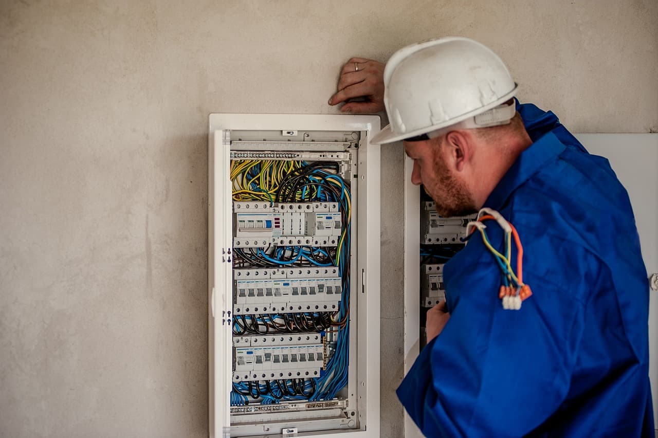 Electrician in a hard hat working inside an open breaker panel